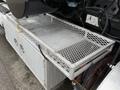 A metal storage compartment mounted on the side of a 2013 International Workstar 7500 featuring a mesh design and a solid base for secure storage