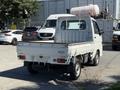 A white 2009 Daihatsu Hijet mini truck with a flatbed and a cabin that has a tall rear window parking in a vehicle lot