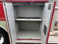 The image shows the open compartment of a 2002 GMC C7500 fire truck with a metal rack in the middle and a textured floor inside