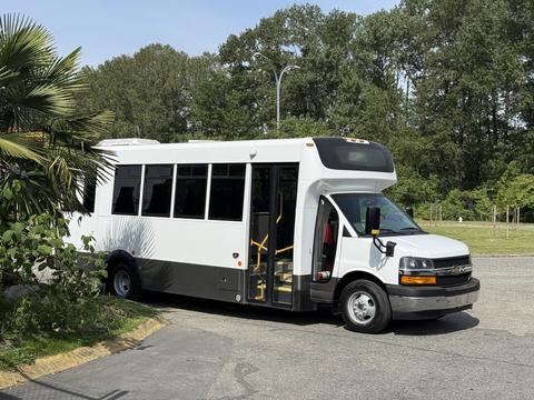 A white 2020 Chevrolet Express bus with large windows and yellow steps is parked, showcasing its spacious interior and modern design