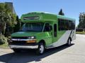 A green and white 2013 Chevrolet Express shuttle bus with large windows and a distinctive front design parked on a road