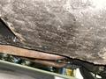 Underside view of a 1968 Ford Mustang showing rusted exhaust pipes and a textured surface with dirt and grime accumulation