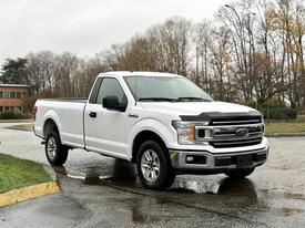 A white 2018 Ford F-150 parked with a single cab and standard bed featuring a chrome front grille and alloy wheels