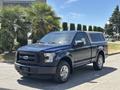 A blue 2015 Ford F-150 with a truck cap parked on a street featuring chrome wheels and a black grille