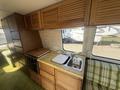Interior of a 1976 GMC Motorhome featuring a wooden kitchen area with cabinets a sink and a small stove against a patterned countertop