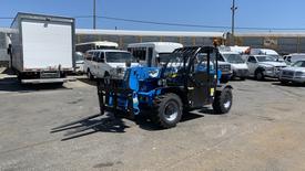 A blue and black 2017 Genie GTH 2506 telehandler with a front-mounted fork attachment positioned for lifting operations