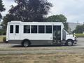 A 2020 Chevrolet Express bus with a white exterior and large windows is parked, featuring an entry door on the side and a sleek van-like appearance