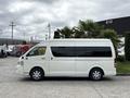 A white 2009 Toyota Hiace van with large windows and a high roof parked beside greenery