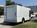 A white 2012 Ford Econoline cargo van with a rear roll-up door and side windows parked on a lot
