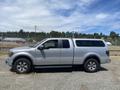 A silver 2014 Ford F-150 pickup truck with a camper shell and off-road tires parked on gravel