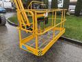 A yellow aerial work platform with a mesh floor and safety railings designed for lifting workers to elevated positions