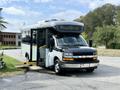 A 2020 Chevrolet Express bus with a black front and white body parked with its side door open and a wheelchair ramp extended
