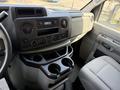 The dashboard of a 2023 Ford E-450 featuring a black display panel with audio controls and climate settings along with cup holders in the center console