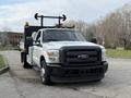 A white 2015 Ford F-350 truck with a black flatbed and orange lights on the roof facing forward in a parking area