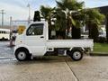 A white 2008 Suzuki Carry truck is parked, featuring a compact cabin and an open cargo bed with a flatbed design and small wheels