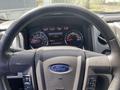 A close-up of the steering wheel and dashboard of a 2014 Ford F-150 displaying gauges and controls with a Ford logo on the steering wheel
