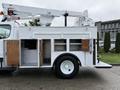 A 2005 Freightliner M2 106 truck with a white exterior features a utility bed with multiple open compartments and a mounted aerial lift mechanism on top