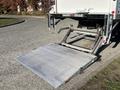 A loading ramp extends from the rear of a truck with a gray surface and metal support arms in a lowered position