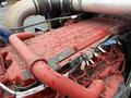 A red engine part of a 2018 Kenworth T800 with various tubes and wires connected to it showing some dirt and debris on the surface