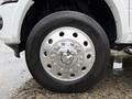 A close-up of a shiny chrome wheel with a circular design and multiple holes on a wet surface, showcasing the 2024 RAM 5500 tire and rim