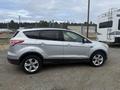 A silver 2014 Ford Escape parked on gravel showing its side profile with five-spoke wheels and a sleek design