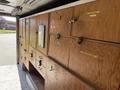 A wooden storage unit with multiple cabinets featuring labeled doors and hooks for various items inside a vehicle