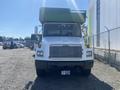 A 1997 Freightliner FL70 truck with a white body and green cargo area visible from the front with a flat nose and a wide windshield