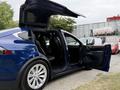 A blue 2020 Tesla Model X with its falcon-wing doors open showcasing the interior seating arrangement and spacious cabin