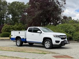 A white 2017 Chevrolet Colorado pickup truck with a blue trim and a utility bed is parked with features like chrome wheels and a front winch