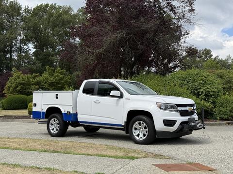 A white 2017 Chevrolet Colorado pickup truck with a blue trim and a utility bed is parked with features like chrome wheels and a front winch