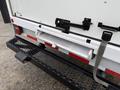 A 2022 Ford E-450 van with a white rear door featuring a retractable step and black metal step platform attached to the back
