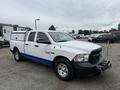 A 2016 RAM 1500 pickup truck with a white exterior and blue accents equipped with a front-mounted winch and a camper shell on the bed