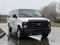 A 2013 Ford E-350 van with a white exterior and black front grille parked on a wet surface with visible headlights and windows
