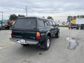 A green 2004 Toyota Tacoma with a truck bed cover parked on a lot showcasing the vehicle's rear view and TRD badge