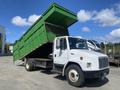 A white 1997 Freightliner FL70 with a green dump truck bed raised, showcasing its large cargo area designed for hauling materials