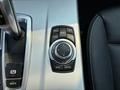 A close-up of the control panel in a 2013 BMW X3 featuring buttons for media, navigation, radio, and options along with a gear shift lever