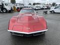 A 1970 Chevrolet Corvette in red with a distinctive hood and sleek design reflecting light rain droplets on its surface