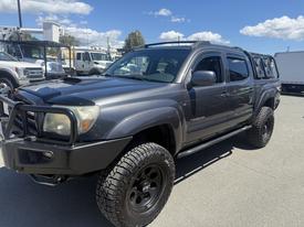 A gray 2010 Toyota Tacoma with off-road tires and a black grill guard parked at a dealership