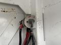 A metallic battery disconnect switch mounted on a white surface with two connected red and black wires above the labeled off position