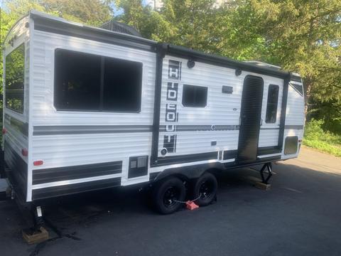 A 2022 Keystone Hide Out RDWE 20RDWE travel trailer with a white and black exterior featuring large windows and a side entry door
