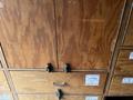 A wooden cabinet with multiple drawers and doors featuring metal handles and labels indicating the contents inside