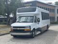 A 2020 Chevrolet Express shuttle bus with a white exterior and gray accents is parked with its door open and accessible steps lowered