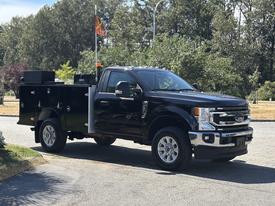 A black 2022 Ford F-350 SD truck with a utility bed featuring toolboxes and an orange warning light on the cab