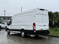 A 2023 Ford Transit van in white with a high roof and cargo area in the rear parked in a wet area