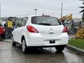 A white 2012 Nissan Versa hatchback parked with its rear view visible showing the logo and model name on the back