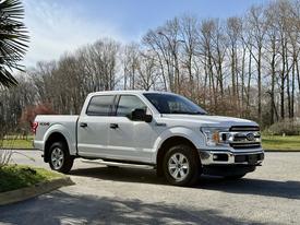 A white 2018 Ford F-150 truck with chrome accents and four doors parked on a gravel driveway