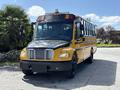 A yellow 2011 Freightliner B2 school bus with a black front grille and dark tires parked with multiple windows along the side