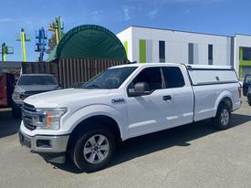 A white 2019 Ford F-150 pickup truck is parked with a truck cap on the bed and features a crew cab design