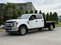 A white 2019 Ford F-350 Super Duty truck with a flatbed and chrome wheels parked on a driveway