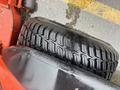 A close-up of a black tire from a 2010 Kubota F3680 featuring a thick tread pattern and mounted on a red frame